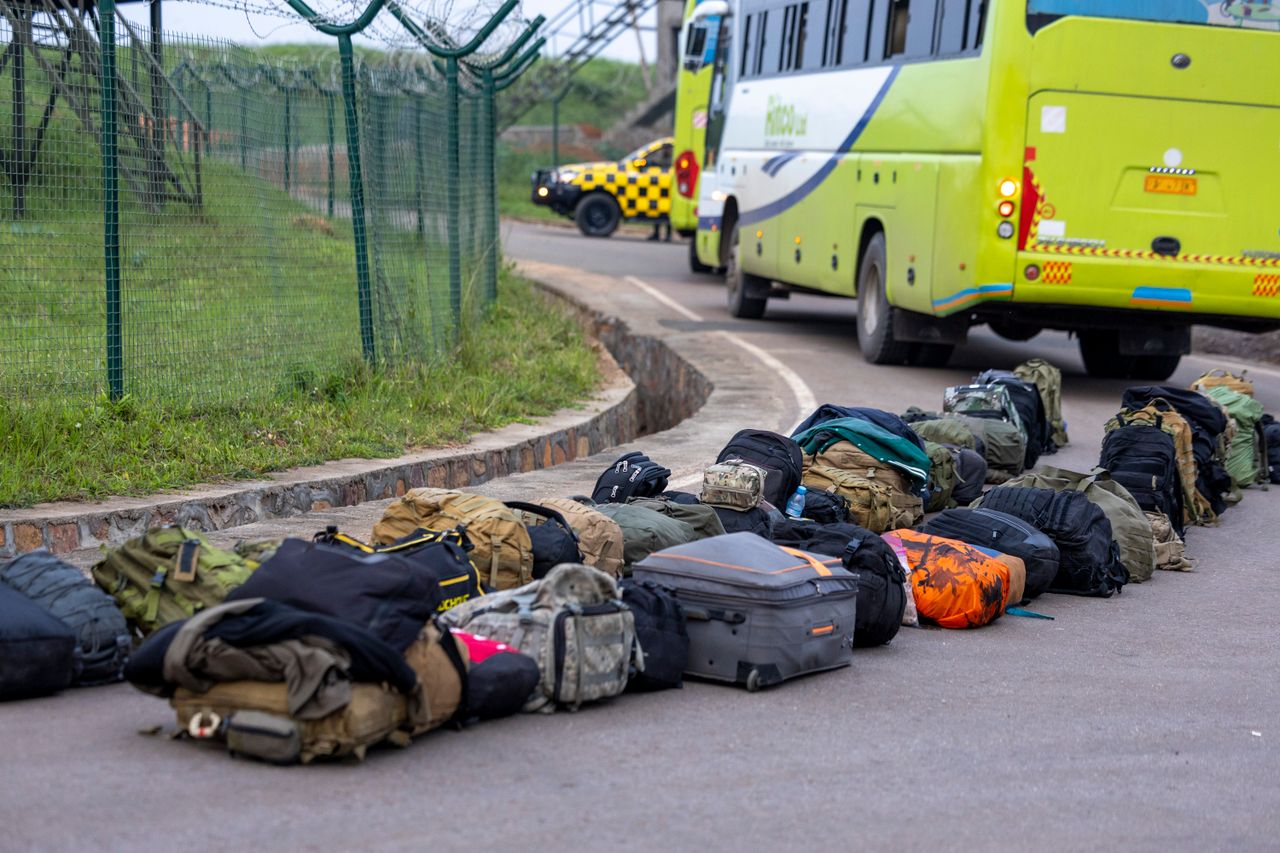 A row of backpacks and luggage near a green bus on a roadway.
